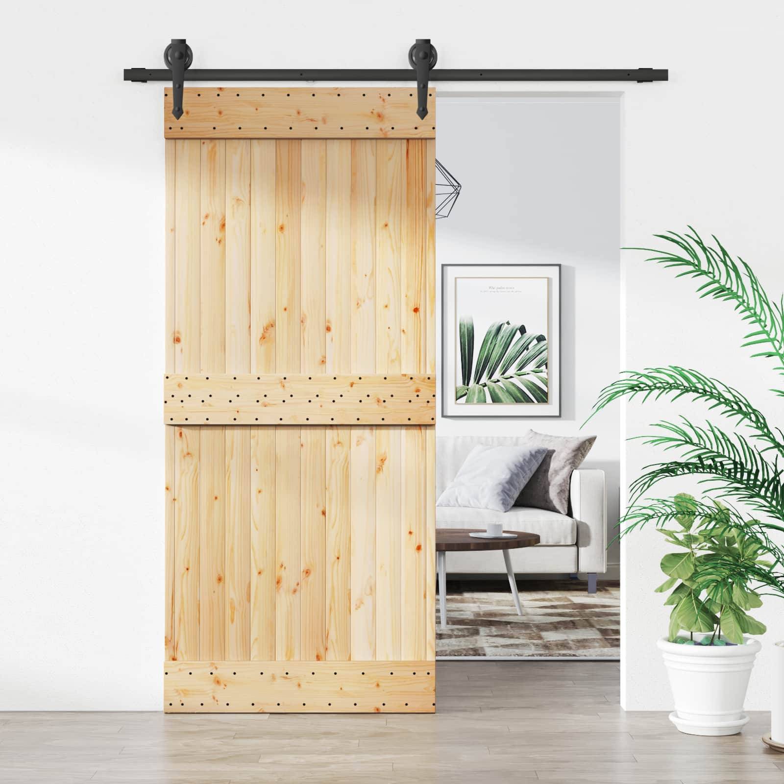 Holztür im Scheunenstil, die teilweise offen ist und einen hellen Wohnzimmer mit Sofa, Bilderrahmen, Teppich und Topfpflanze zeigt.