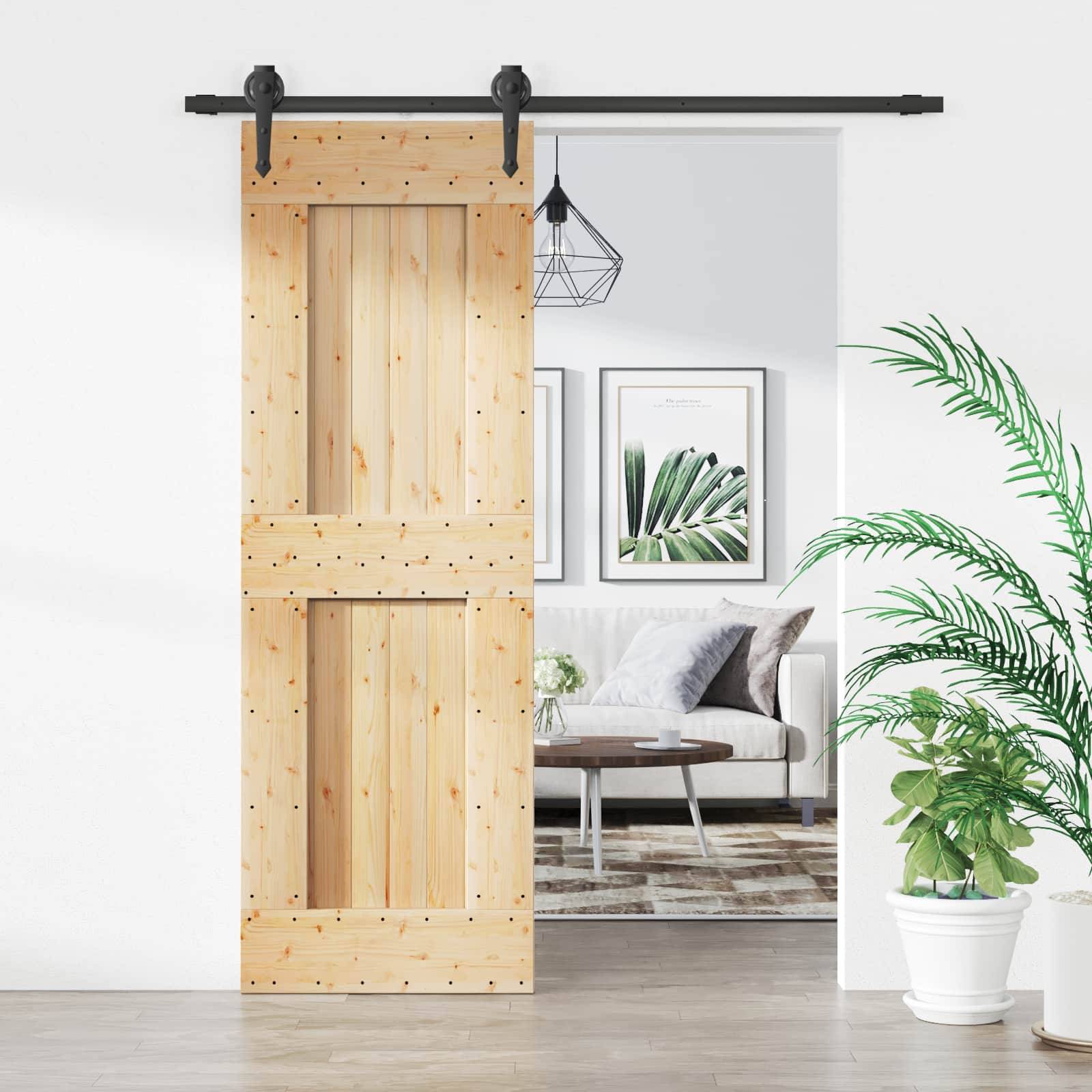 Holztür im Scheunenstil, teilweise offen, mit Blick auf ein helles, modernes Wohnzimmer mit Sofa, Couchtisch, gerahmten Kunstwerken, hängender Leuchte und Topfpflanzen.