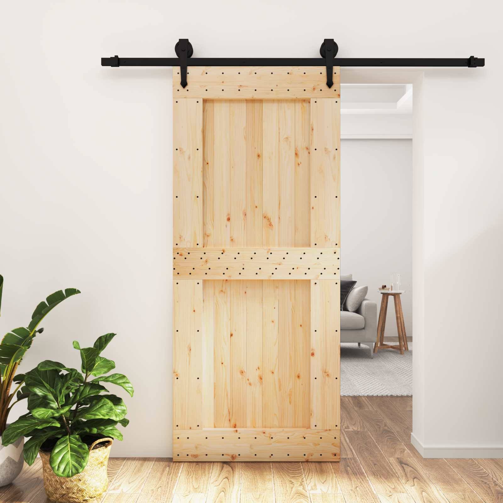 Eine hölzerne Schiebescheunentür mit schwarzer Beschlagteile ist in einem hellen Wohnungsinterieur teilweise geöffnet und gibt den Blick auf ein dahinter liegendes Wohnzimmer frei.
