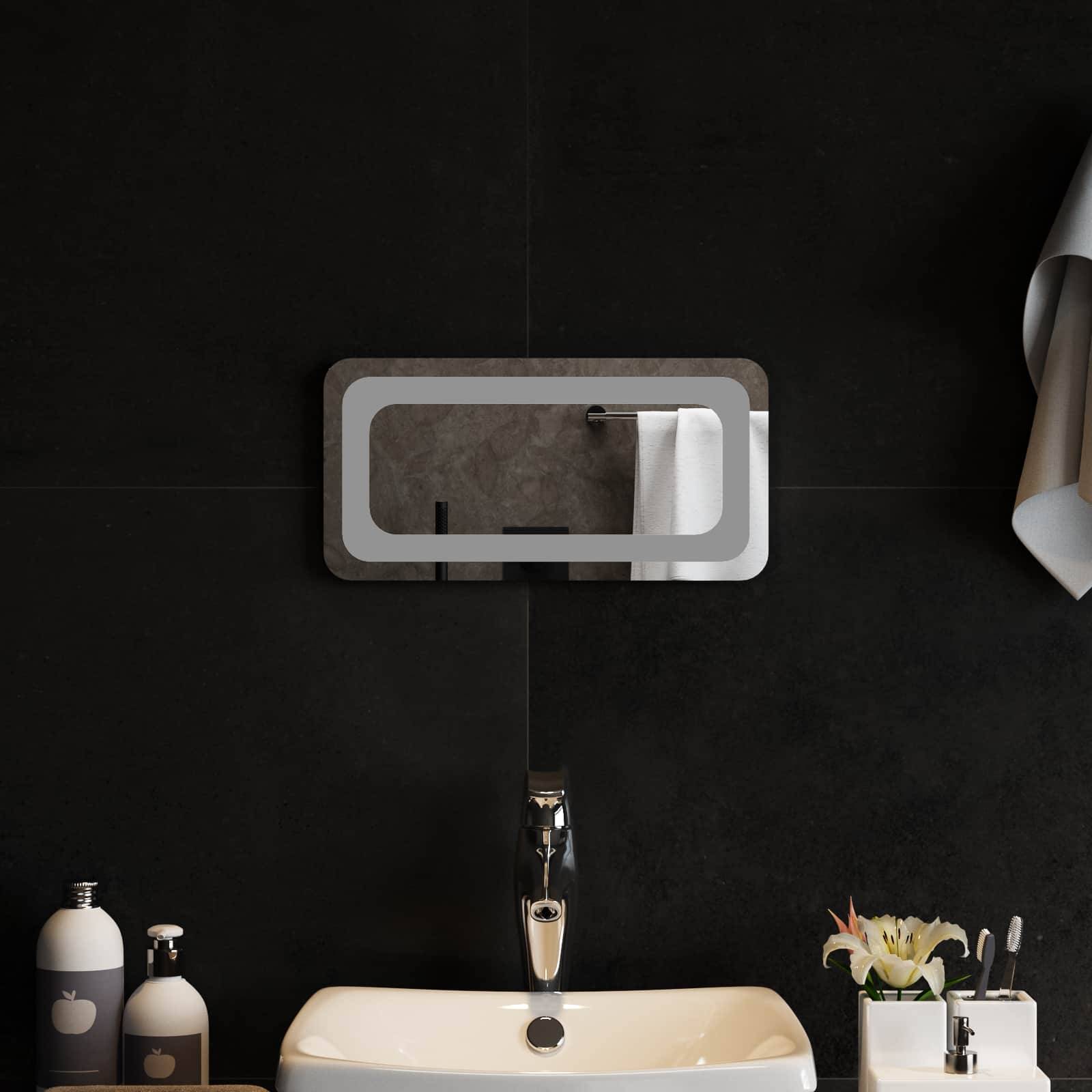 Modernes Badezimmer-Waschbecken mit wandmontierten Spiegelschrank, Armatur, Seifenspendern und Blumenvase vor einer dunkel gefliesten Wand.