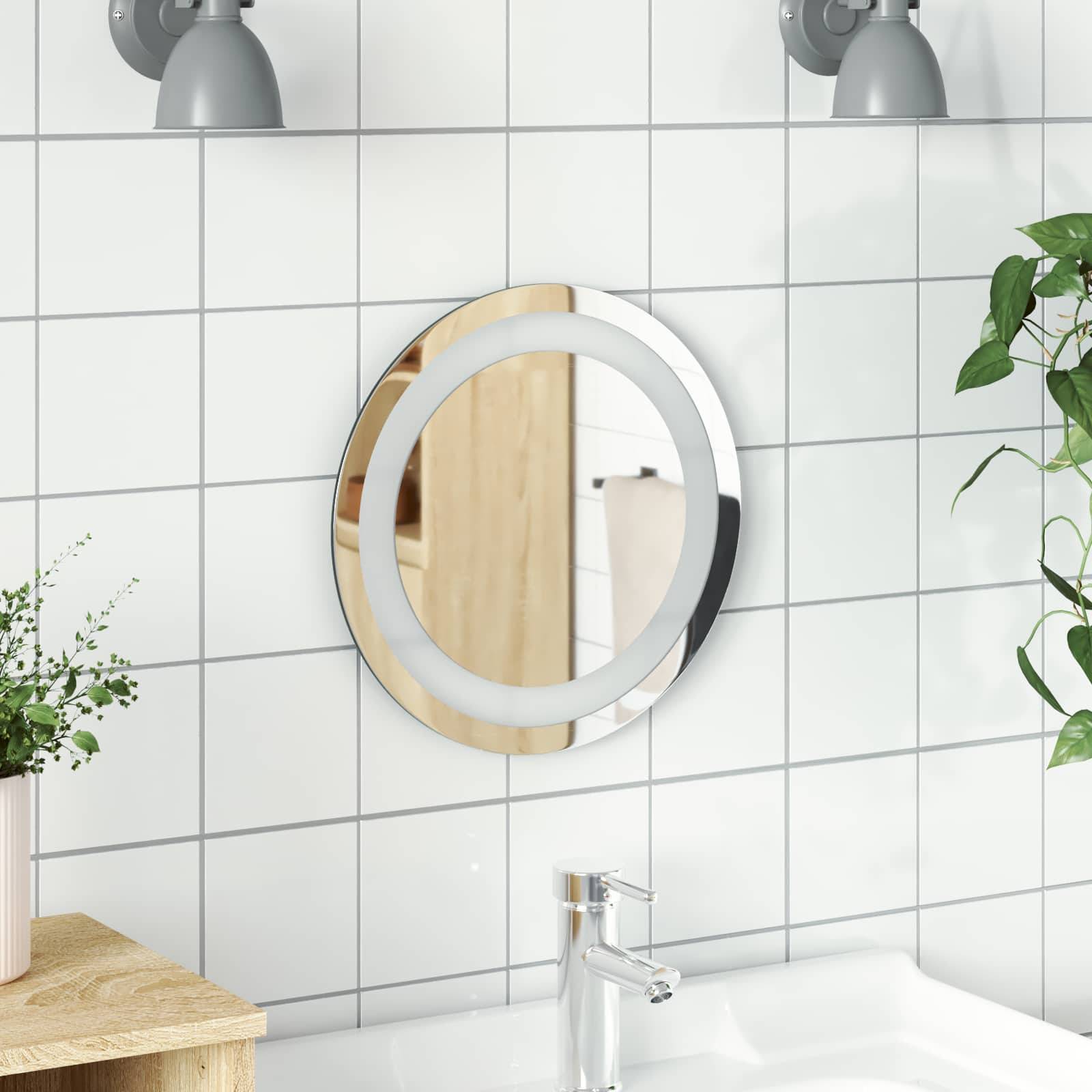 Moderner Waschbereich im Badezimmer mit rundem beleuchteten Spiegel an weißer gekachelter Wand über einem Chromhahn und Arbeitsflächendekoration.