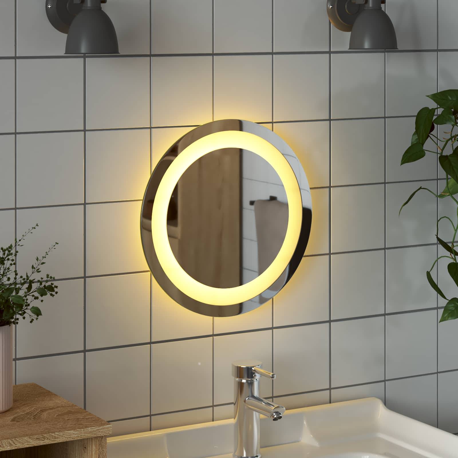 Runder beleuchteter Badezimmerspiegel über einem Waschbecken und Wasserhahn an einer gekachelten Wand, mit warmem Licht, das sich im Spiegel spiegelt.
