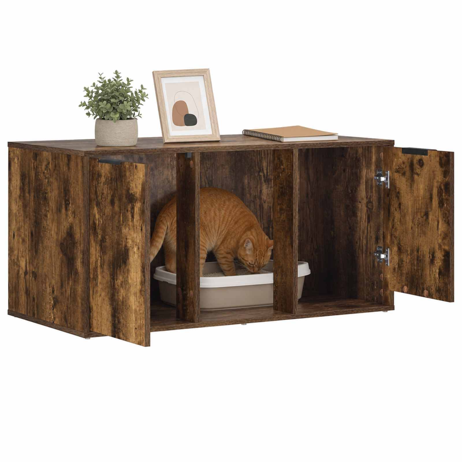Orangefarbene Katze, die eine versteckte Katzentoilette in einem rustikalen Holzschrank mit offenen Türen benutzt; eine Pflanze, ein gerahmtes Kunstwerk und ein Buch sitzen oben darauf.