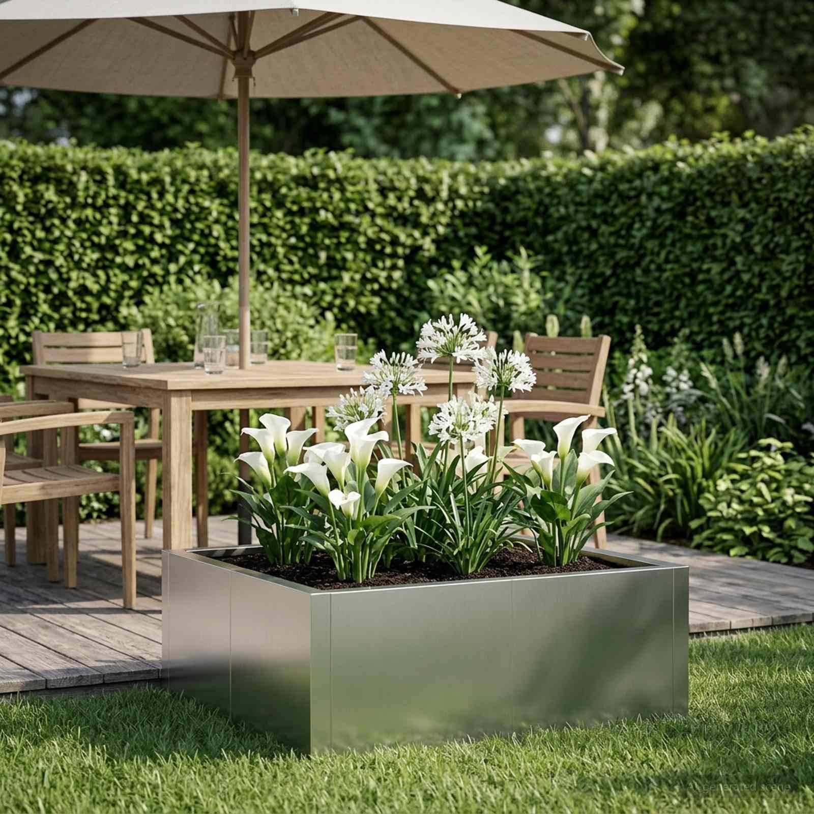Terrassengarten mit einem Metallkübel weißer Blumen vor einem Holztisch, Stühlen und einem Schirm auf einer Terrasse neben einer Hecke.
