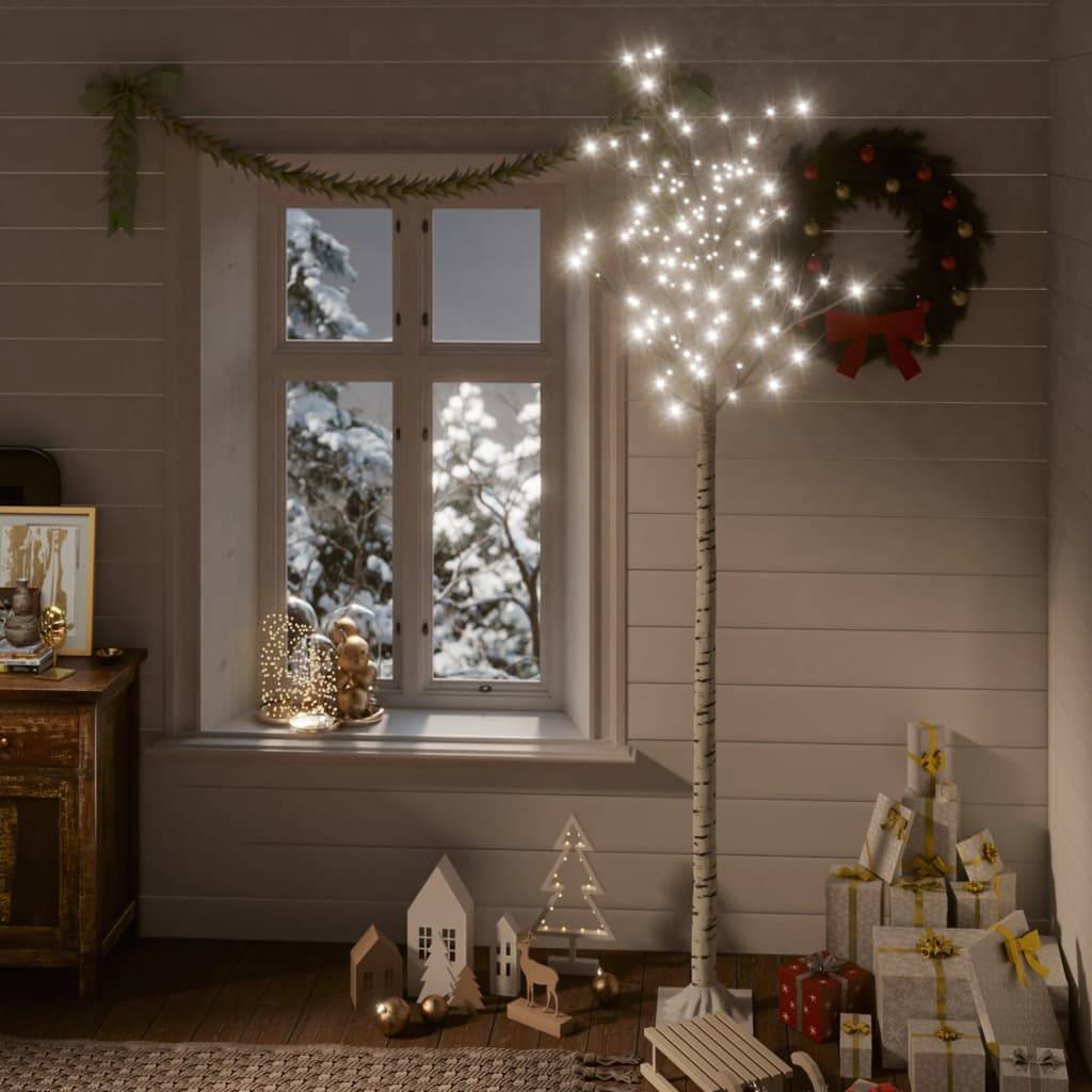 Gemütliches Ferienszimmer mit einem beleuchteten dekorativen Birkenbaum, Kranz, schneebedeckter Fensterszene und gestapelten verpackten Geschenken neben kleiner hölzerner Weihnachtsdorfdekoation.