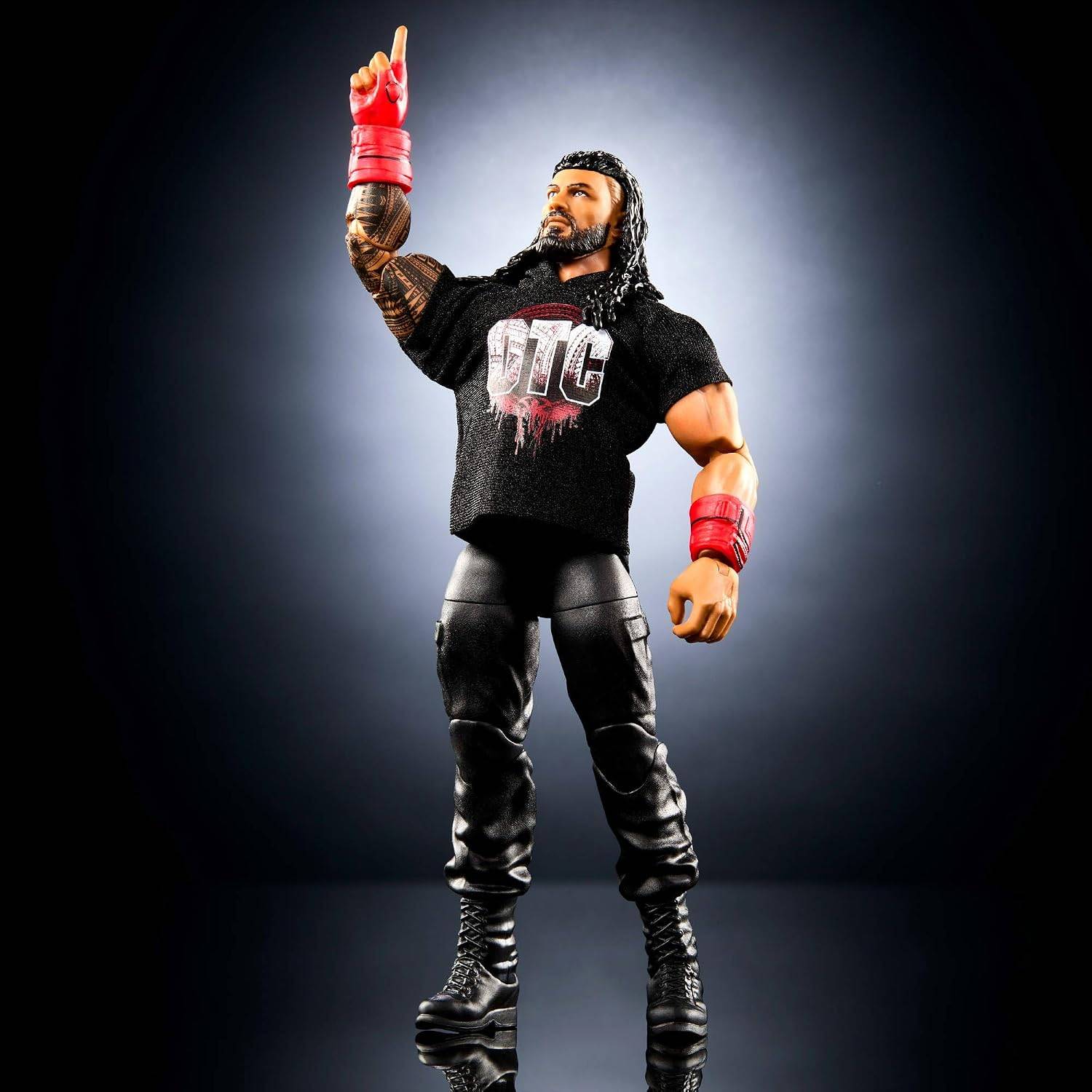 Actionfigur eines muskulösen Mannes in schwarzer Hose und schwarzem 'DIC' T-Shirt, mit langen schwarzen Haaren und roten Armbändern, die gegen einen dunklen Hintergrund nach oben zeigt.