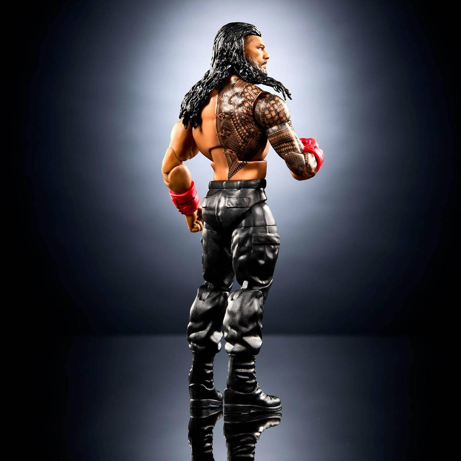 Eine muskulöse Actionfigur mit langen schwarzen Haaren und roten Handschuhen, von hinten gezeigt in schwarzen Hosen vor einem dunklen Studiohintergrund.