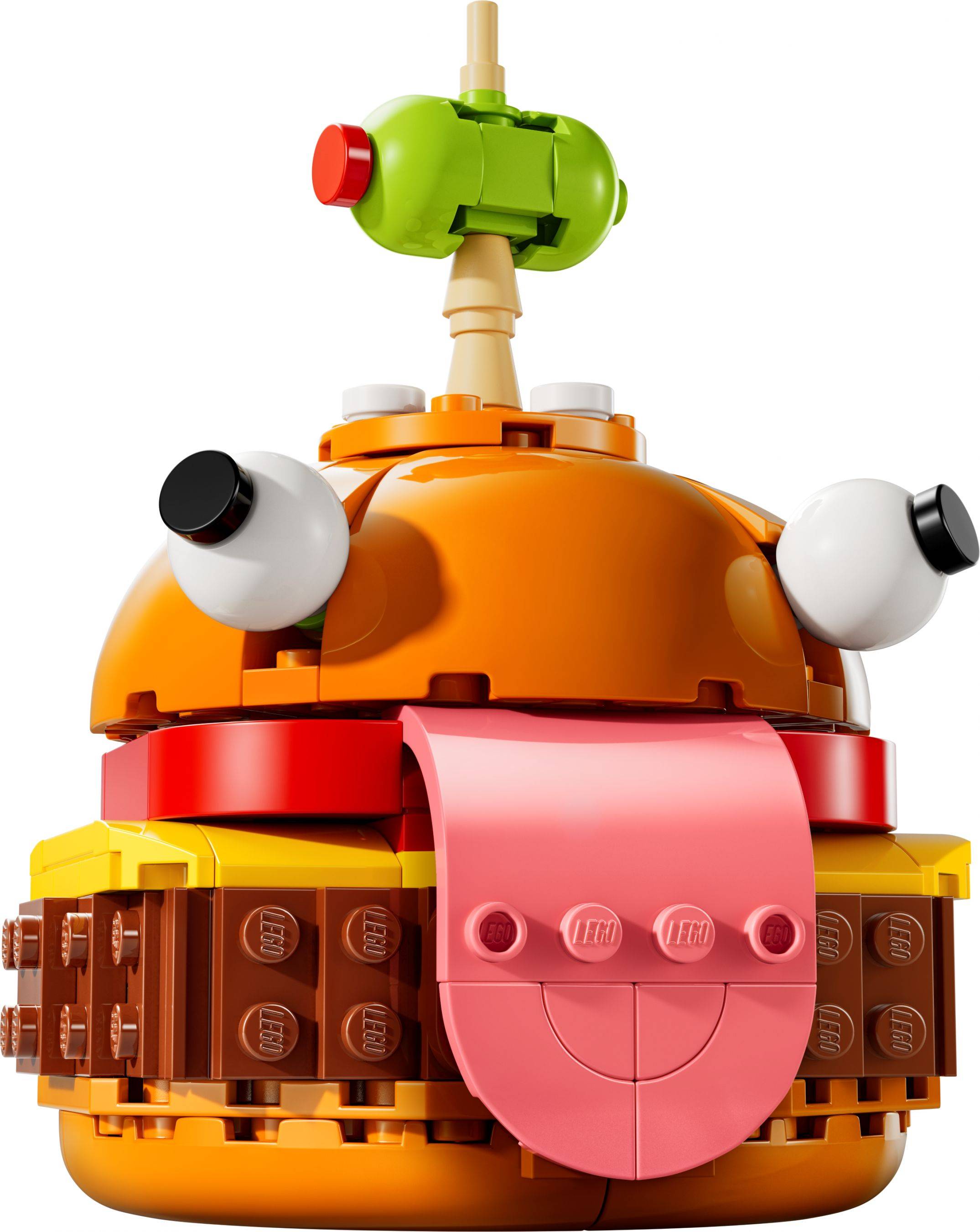 Spielzeug-Hamburger-förmiger Roboter mit gelbem Brötchen, oranger Kuppel, rosa Zunge, Wackelaugen und einer grünen Antenne auf weißem Hintergrund