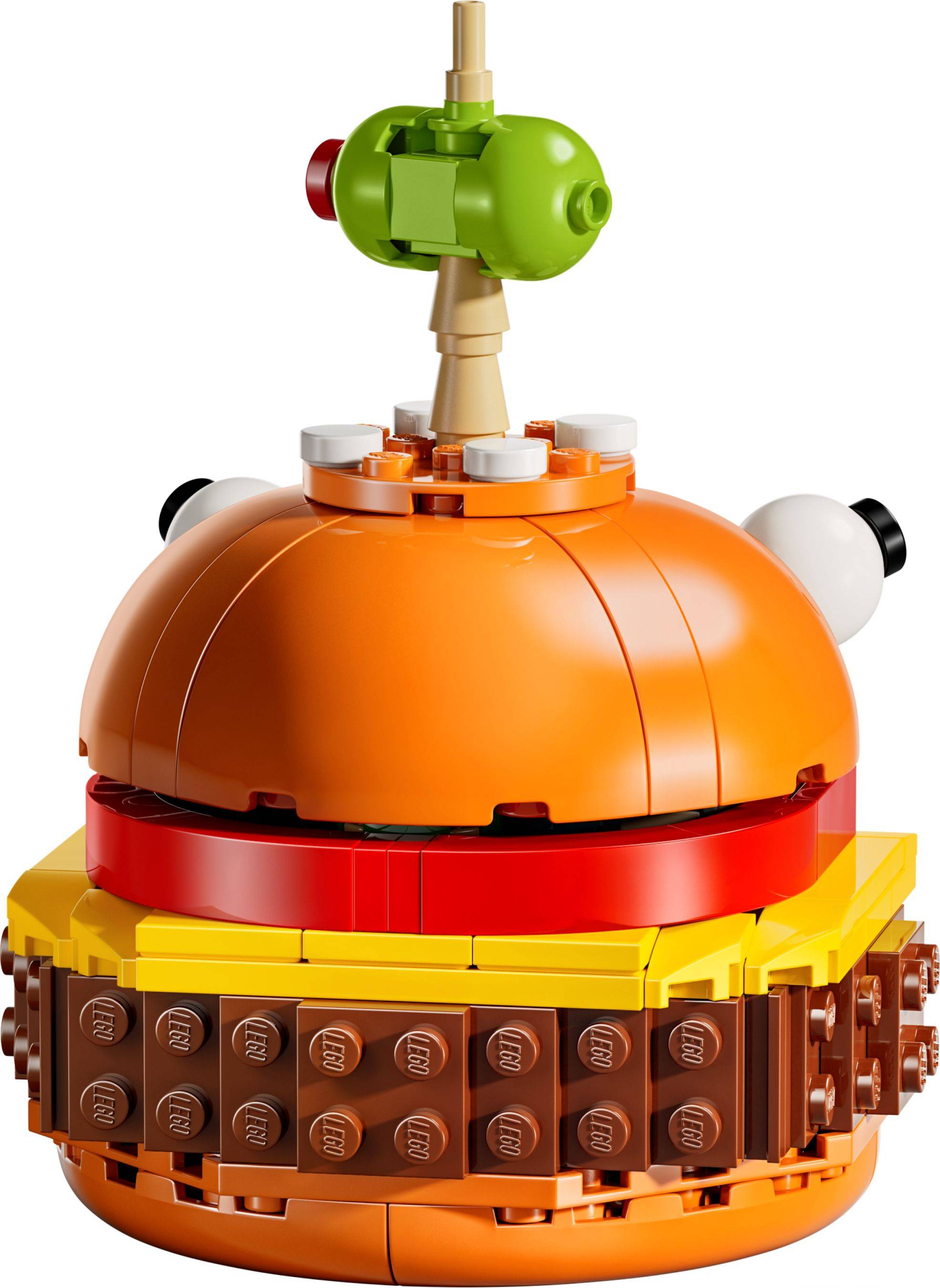 LEGO-ähnliches orangefarbenes burger-förmiges Modell mit einem Brötchen, Salat- und Tomatenschichten, gekrönt durch eine kleine grüne Figur oder Garnitur auf einem Stab.