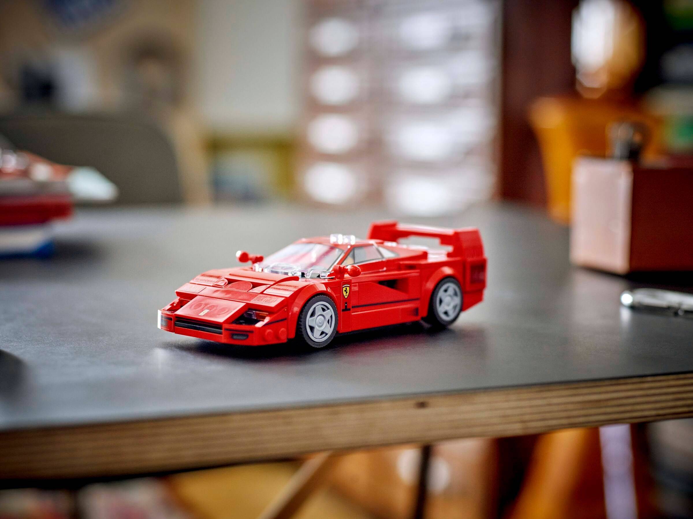 Rotes LEGO-ähnliches Sportwagenmodell auf einer Tischplatte, in Großaufnahme mit verschwommenem Innenraum-Hintergrund gezeigt.