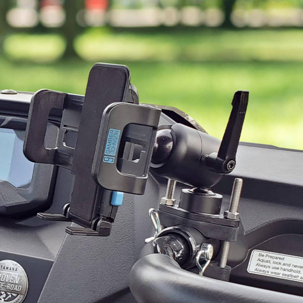 Telefon in einer robusten Fahrzeughalterung auf dem Armaturenbrett montiert, mit einer verstellbaren Klammer und einem Drehknopf in der Nähe eines Windschutzscheiben-Sicherheitsaufklebers.