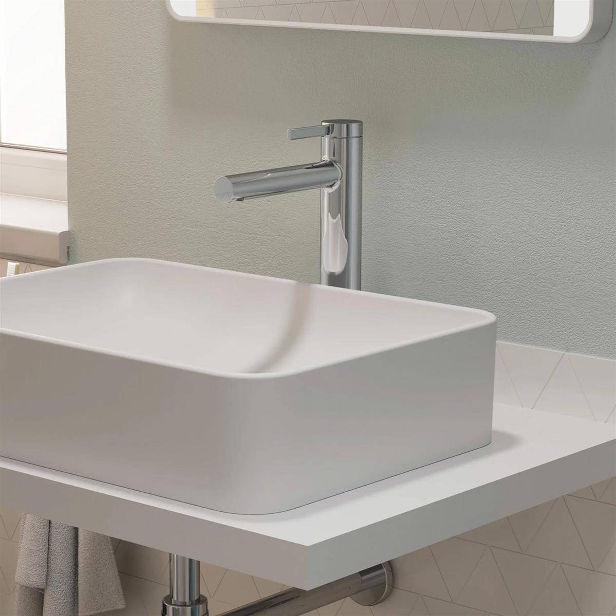 Modernes weißes Waschbecken mit Chromarmatur auf einer weißen Arbeitsplatte in einem minimalistischen Badezimmer.