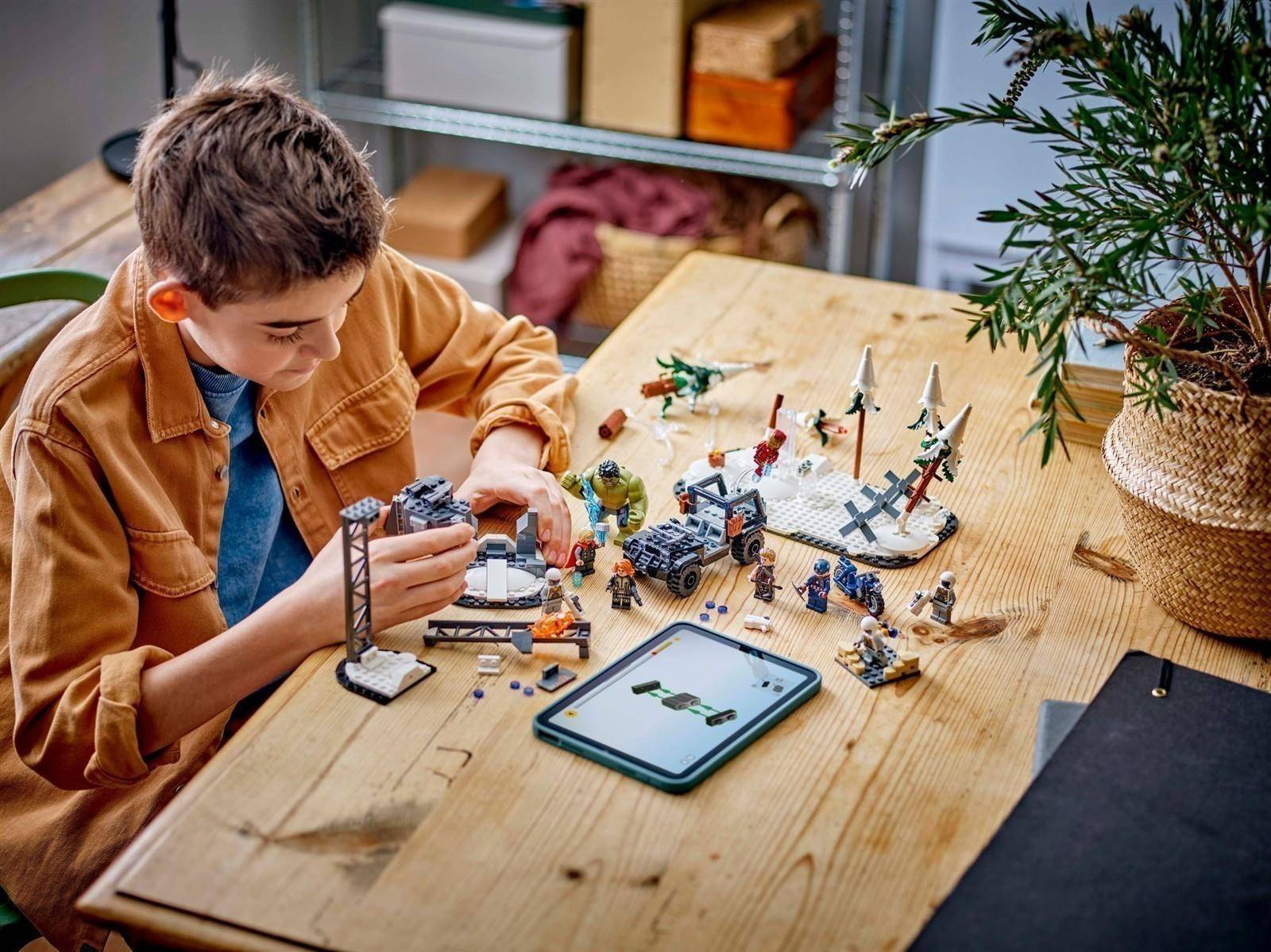 Junge, der ein LEGO-ähnliches Weltraum-Set an einem Holztisch zusammenbaut, nutzt ein Tablet für Anleitung, mit verstreuten Teilen und fertiggestellten Modellen um ihn herum.