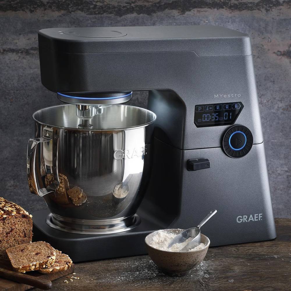 Ein schwarzer Graef Myestro Standmixer mit Edelstahlschüssel, ausgestellt mit geschnittenem Brot und einer kleinen Schüssel Mehl auf einer rustikalen Arbeitsplatte.