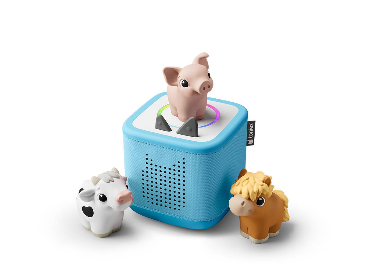 Ein blauer würfelförmiger Lautsprecher mit einer Schweinefigur oben drauf, flankiert von kleinen Kuh- und Pferdefiguren, auf schwarzem Hintergrund.