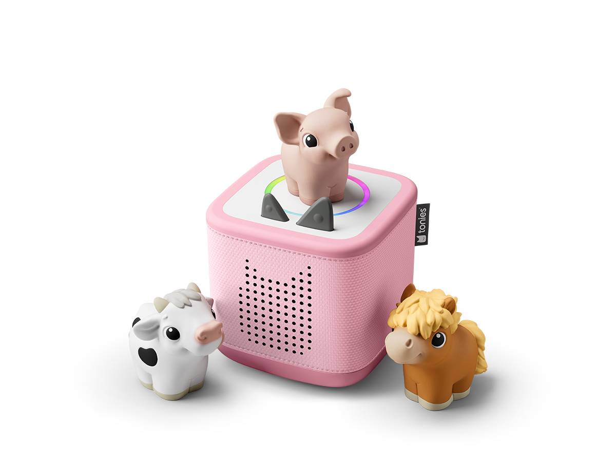 Rosa würfelförmiger Spielzeuglautsprecher mit einer Schweinefigur oben drauf und kleinen Kuh- und Pferdefiguren daneben auf schwarzem Hintergrund.
