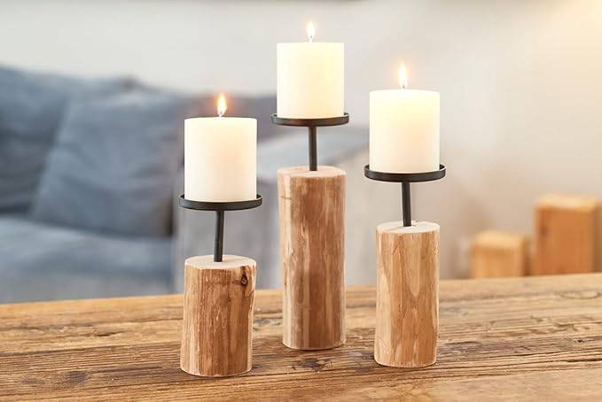 Drei brennende weiße Säulenkerzen auf rustikalen Holzhaltern, die auf einem Holztisch arrangiert sind.
