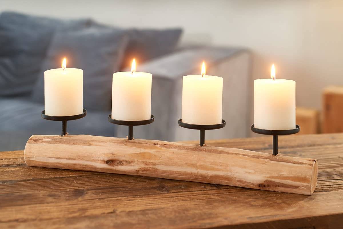 Vier brennende weiße Kerzen in schwarzen Kerzenhaltern auf einem gebogenen Holzständer, arrangiert auf einem rustikalen Tisch mit unscharfem Hintergrund.