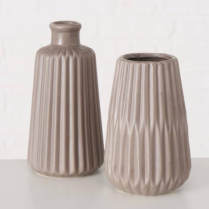 Zwei beige gerippte Keramikvase, eine hohe mit schmalem Hals und eine kürzere Vase mit offener Oberseite, vor einem neutralen Hintergrund dargestellt.