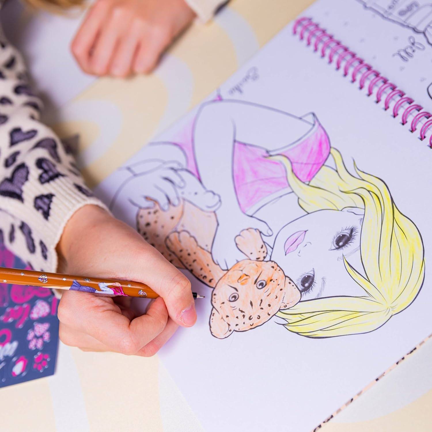 Ein Kind koloriert ein Cartoon-Mädchen in einem Spiralblock mit einem Bleistift und füllt einen rosa Badeanzug und gelbes Haar aus.