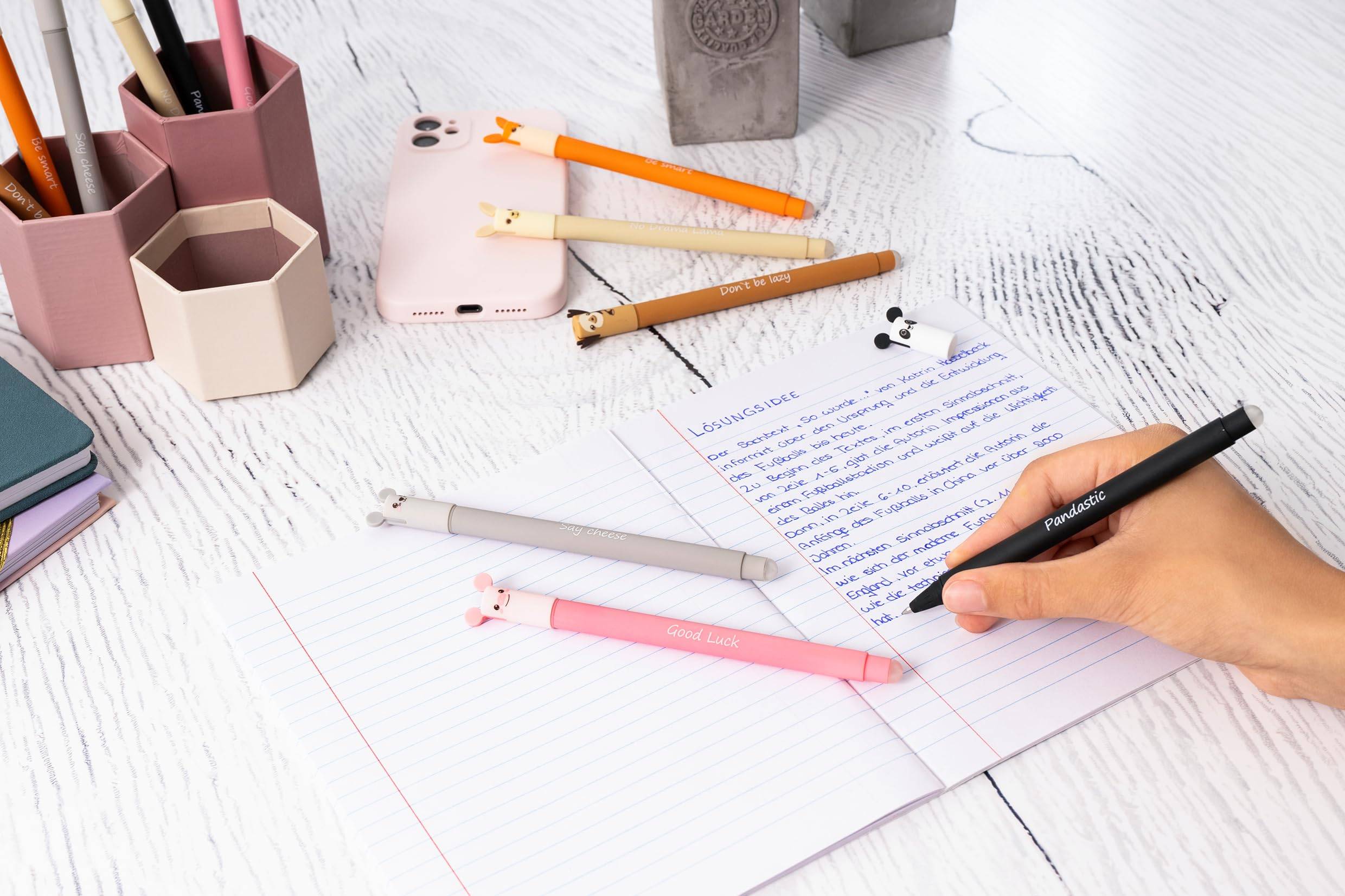 Handschriftliche Notizen in einem Spiralblock mit einem schwarzen Stift neben pastellfarbener Büroausstattung auf einem weißen Schreibtisch.