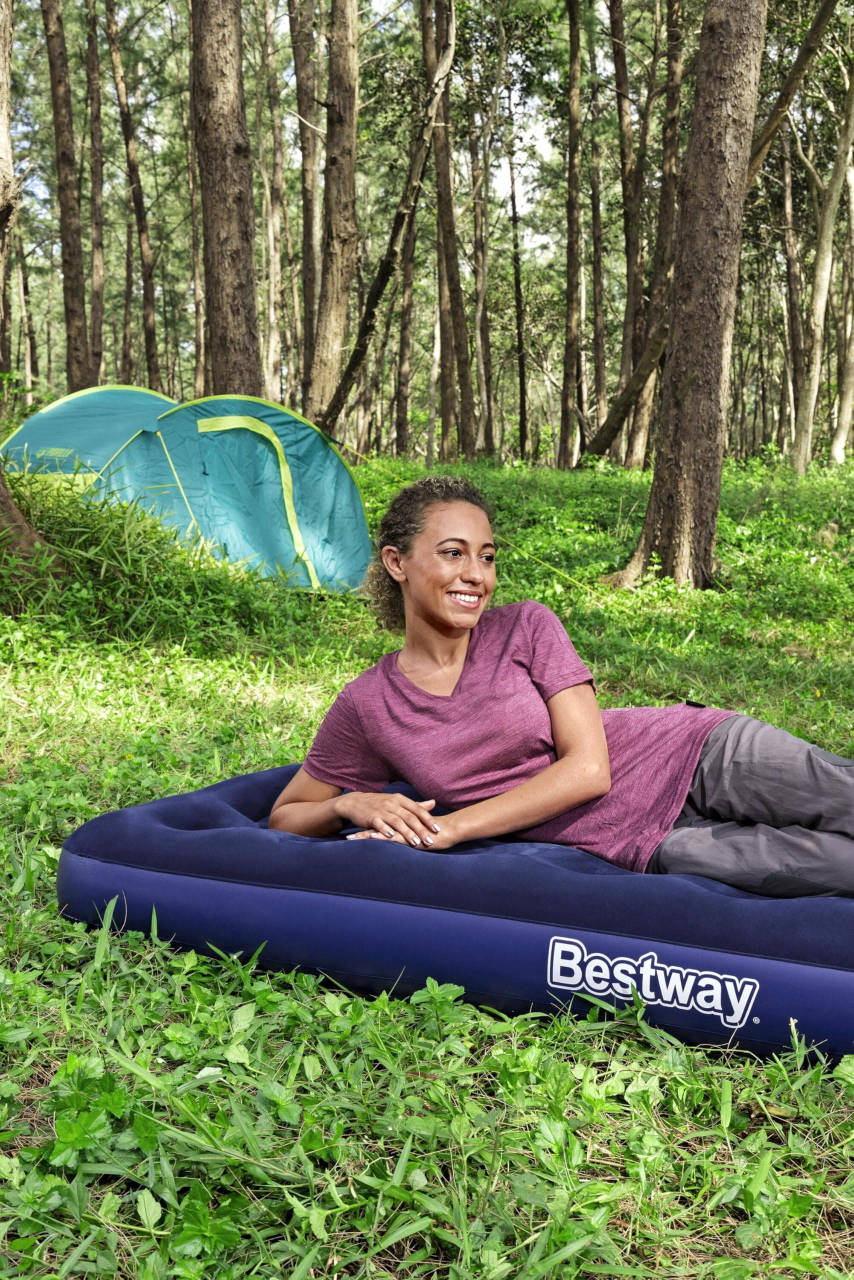 Frau relaxt auf einer Luftmatratze auf einem bewaldeten Campingplatz, mit einem kleinen blauen Zelt hinter ihr und 