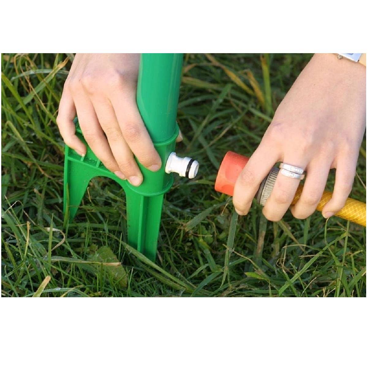 Hände befestigen einen Gartenschlauch an einem grünen Sprinklerstab im Gras.