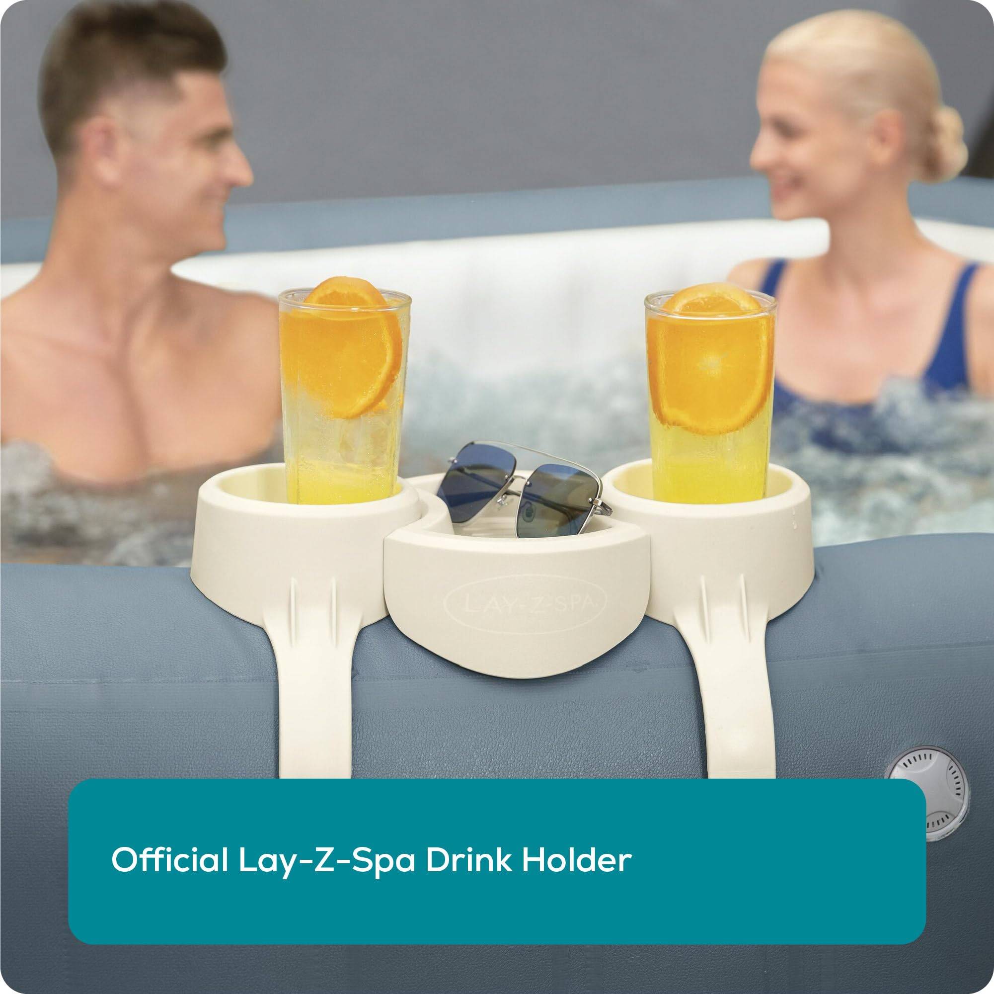 Lay-Z-Spa Getränkehalter mit zwei Cocktails und Sonnenbrille auf dem Rand eines Whirlpools, mit einem Paar, das sich im Hintergrund entspannt.
