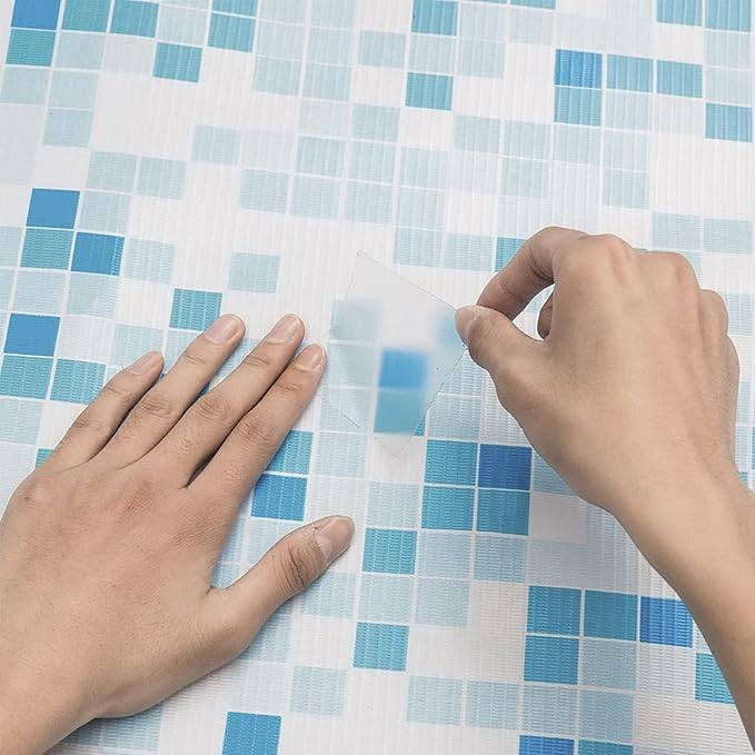 Hände schälen einen transparenten Schutzfilm von einer blau-weißen Mosaikfliesenfläche ab.