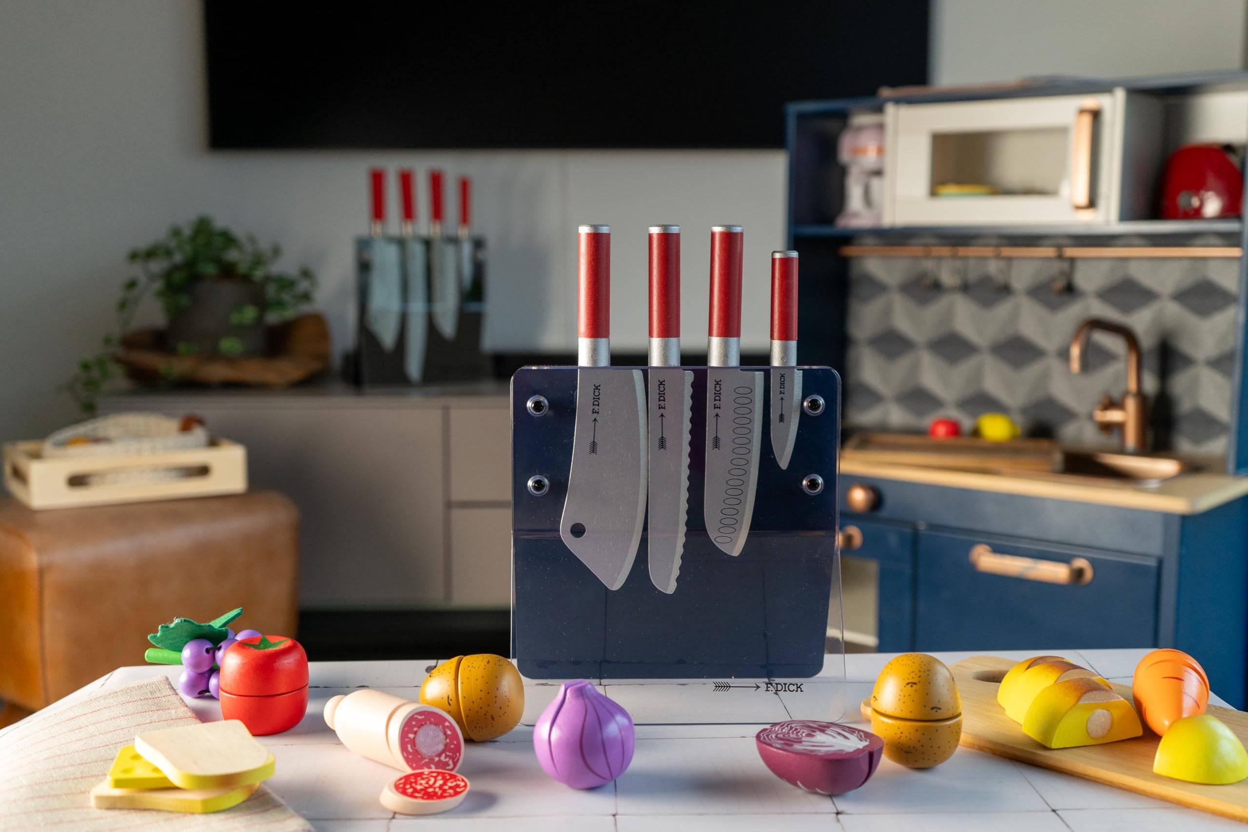 Drei Küchenmesser hängen in einem Messerblock auf einer Arbeitsplatte, umgeben von farbenfrohem, spielzeugähnlichem Obst und Gemüse in einer Küchenumgebung.