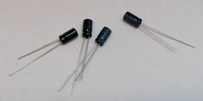 Vier kleine zylindrische elektronische Kondensatoren mit Drahtanschlüssen auf einer einfachen hellen Oberfläche.