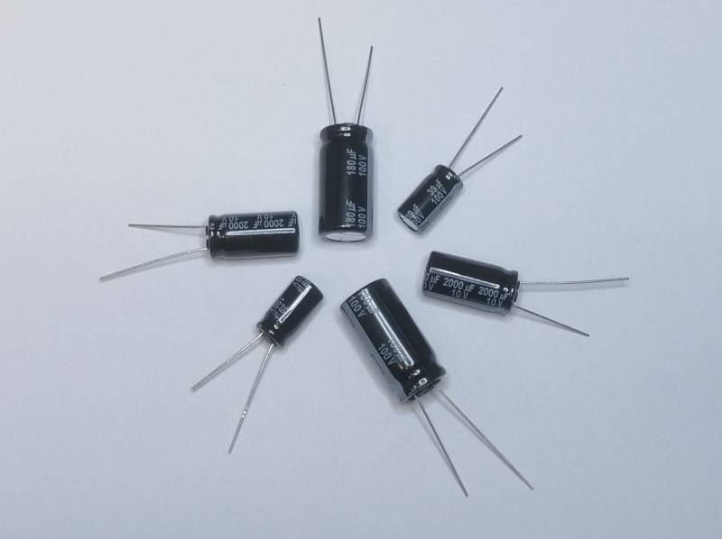 Fünf schwarze Elektrolytkondensatoren mit jeweils zwei Anschlüssen auf einem einfachen hellen Hintergrund angeordnet.