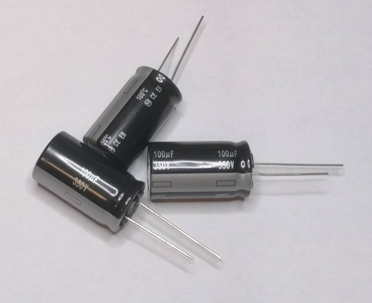 Drei schwarze zylindrische Elektrolytkondensatoren mit Metallanschlüssen, mit der Aufschrift 100µF und 500V, auf einer weißen Oberfläche angeordnet.
