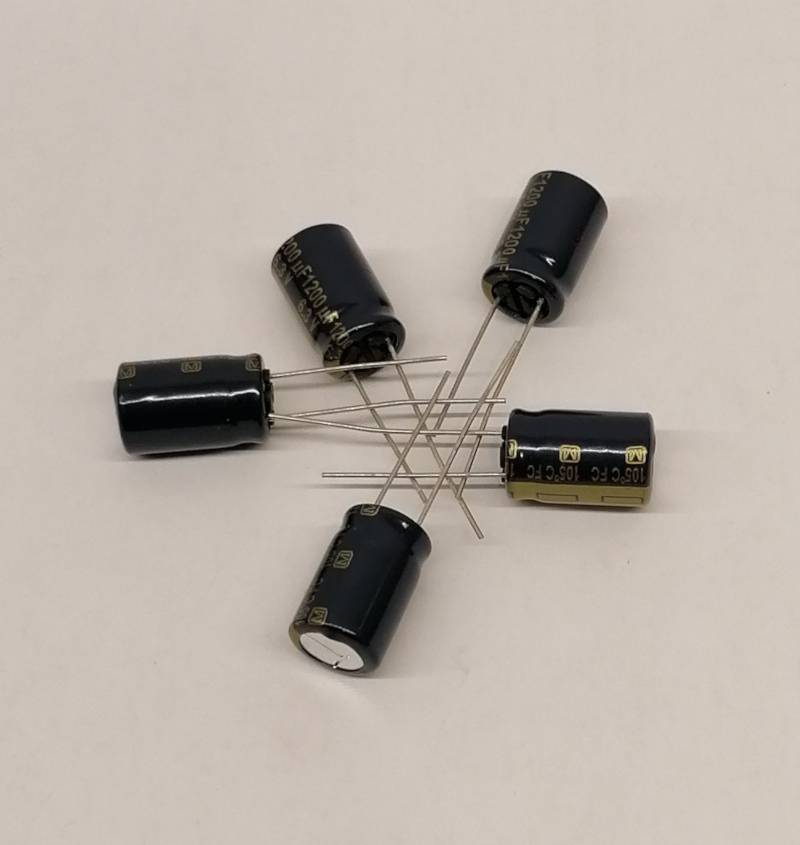 Fünf schwarze zylindrische Elektrolytkondensatoren mit langen Metalldrähten, die in einem sternähnlichen Haufen auf einer einfachen weißen Oberfläche angeordnet sind.