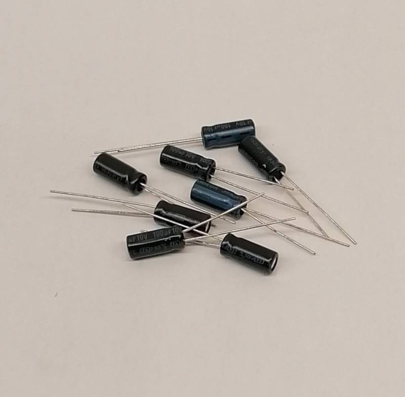 Mehrere kleine zylindrische Kondensatoren mit Metallanschlüssen verstreut auf einer hellen ebenen Oberfläche.