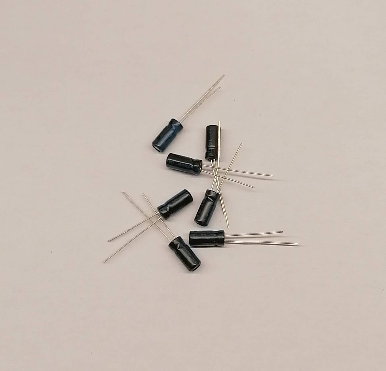 Kleine schwarze elektronische Kondensatoren mit dünnen Drahtanschlüssen, verstreut auf einer ebenen hellen Oberfläche.