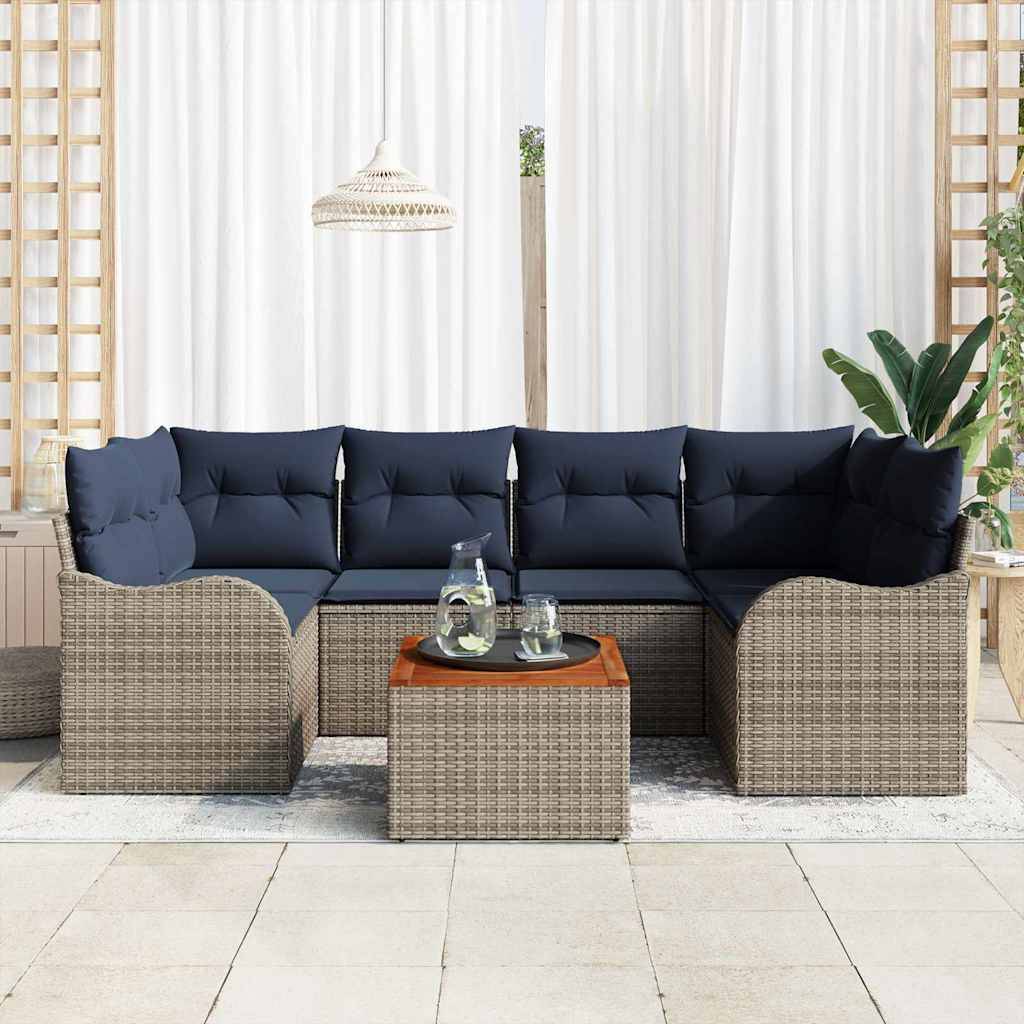 Flechtwerk-Außenecksofa mit marineblauen Kissen, passendem Hocker und Glastisch auf einer Terrasse mit weißen Vorhängen und Pflanzen.