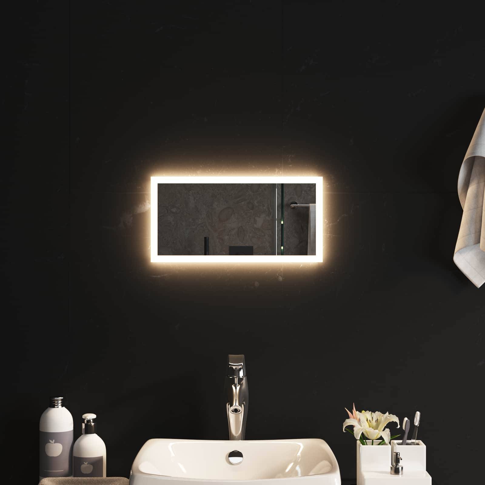Modernes Badezimmerwaschtisch mit hinterleuchtitem rechteckigem Spiegel über einem weißen Waschbecken, flankiert von Seifenspendern und Toilettenartikeln, mit einem Handtuch auf der rechten Seite.