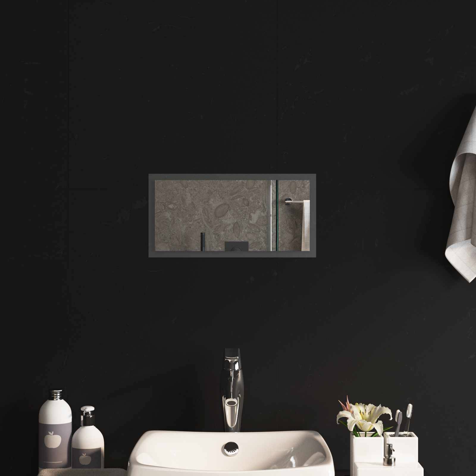 Minimales Badezimmermöbel mit weißem Waschbecken, verchromtem Wasserhahn, Flaschen auf der Arbeitsplatte und einem Spiegel in einem Zimmer mit schwarzen Wänden.