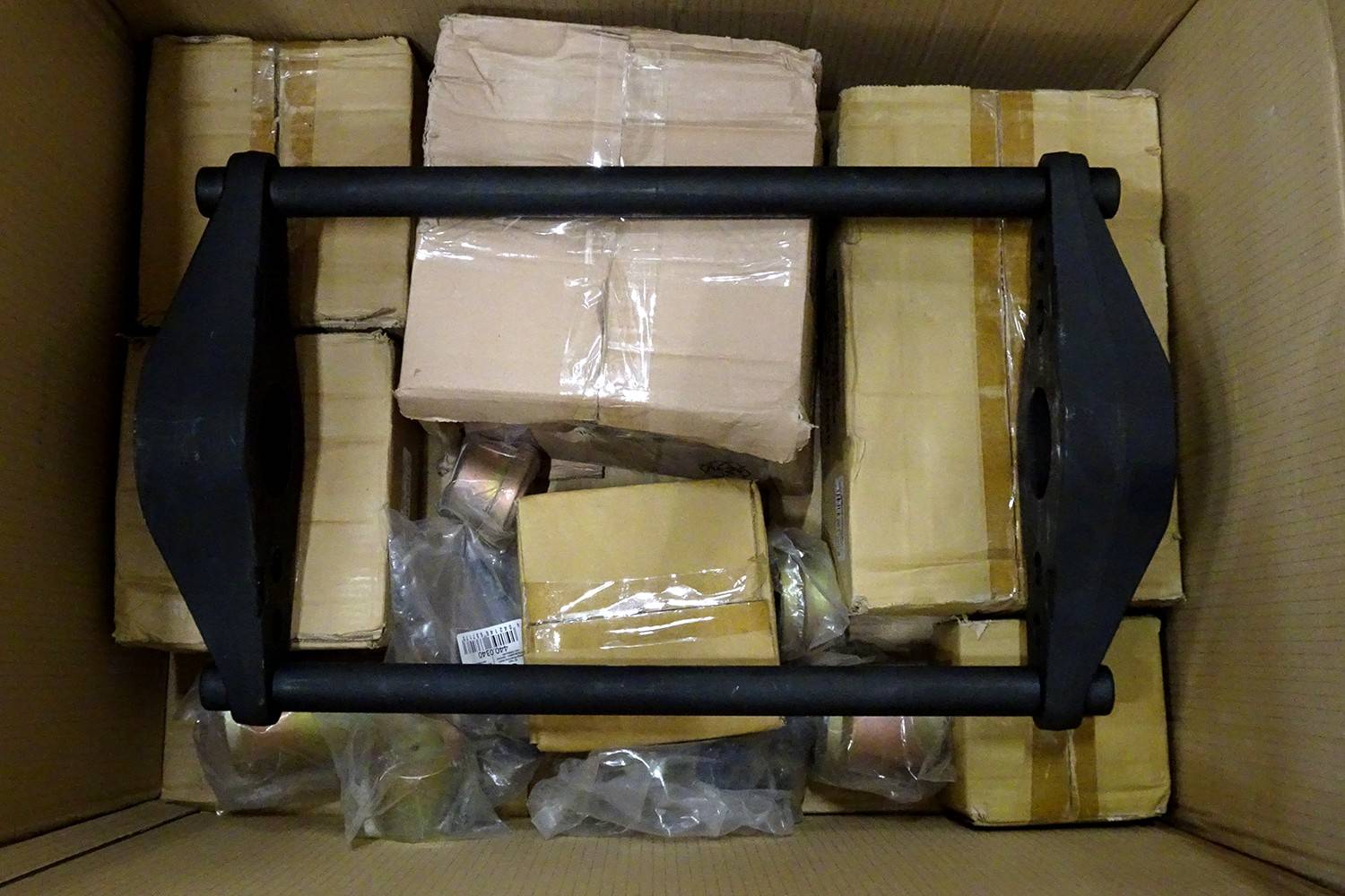 Draufsicht auf einen Kartonversandkarton, der mit verpackten Paketen gefüllt ist, und ein schwarzes Metallgriff-ähnliches Rahmenwerk auf der Oberseite.