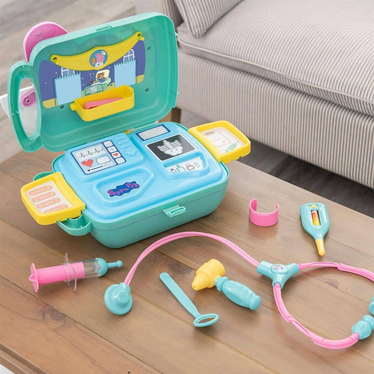 Kinderarztkofferset, das auf einem Tisch offen liegt, mit Stethoskop, Spritze, Thermometer und anderen Spielzeug-Medizininstrumenten neben einem Sofa.