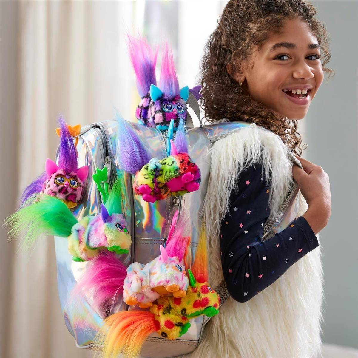 Lächelndes Mädchen, das eine flauschige Weste und einen Rucksack mit bunten Plüsch-Monstergesichtern mit Regenbogenhaar trägt.