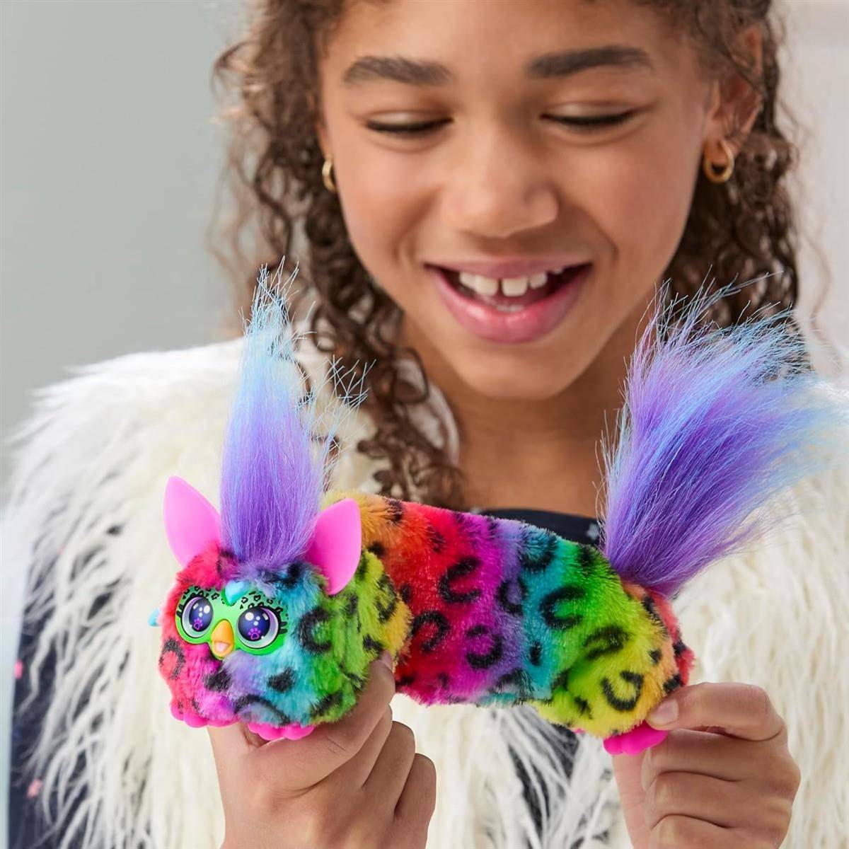 Ein lächelndes Kind hält eine Regenbogen-Leoparden-Muster-Spielzeugkatze mit violettem Fell in beiden Händen.