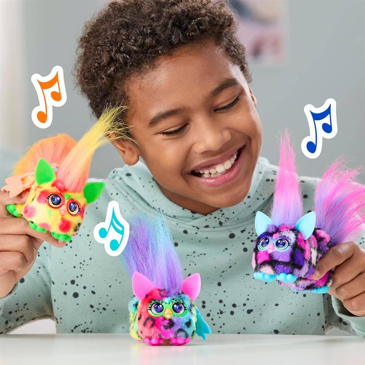 Lachendes Kind, das drei bunte Furby-Spielzeuge hält, deutet auf verspielte, musikthemenbezogene elektronische Spielzeuge hin.