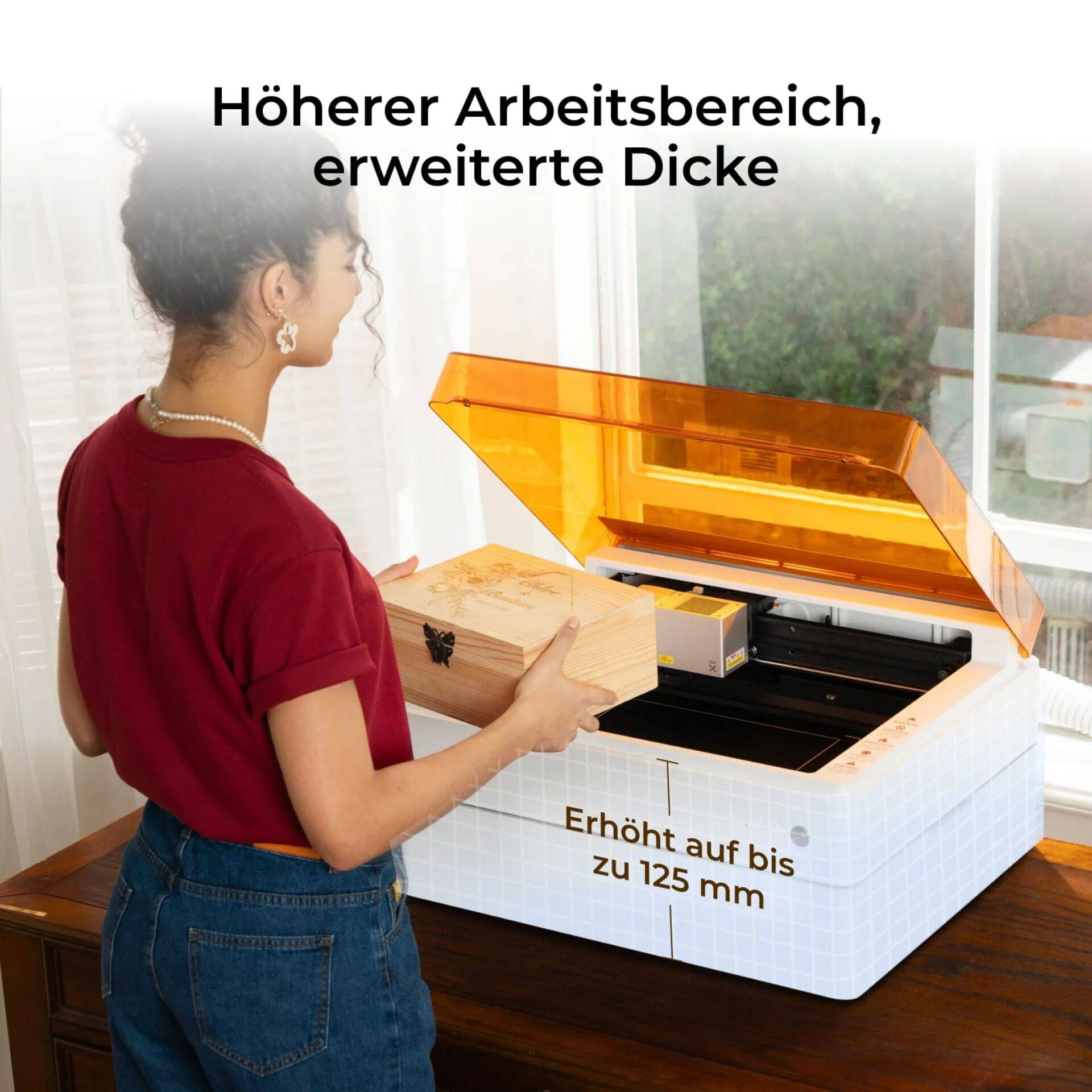 Frau lädt einen großen Holzblock in eine offene Maschine mit orangefarbenem Deckel; der Text besagt „Höherer Arbeitsbereich, erweiterte Dicke