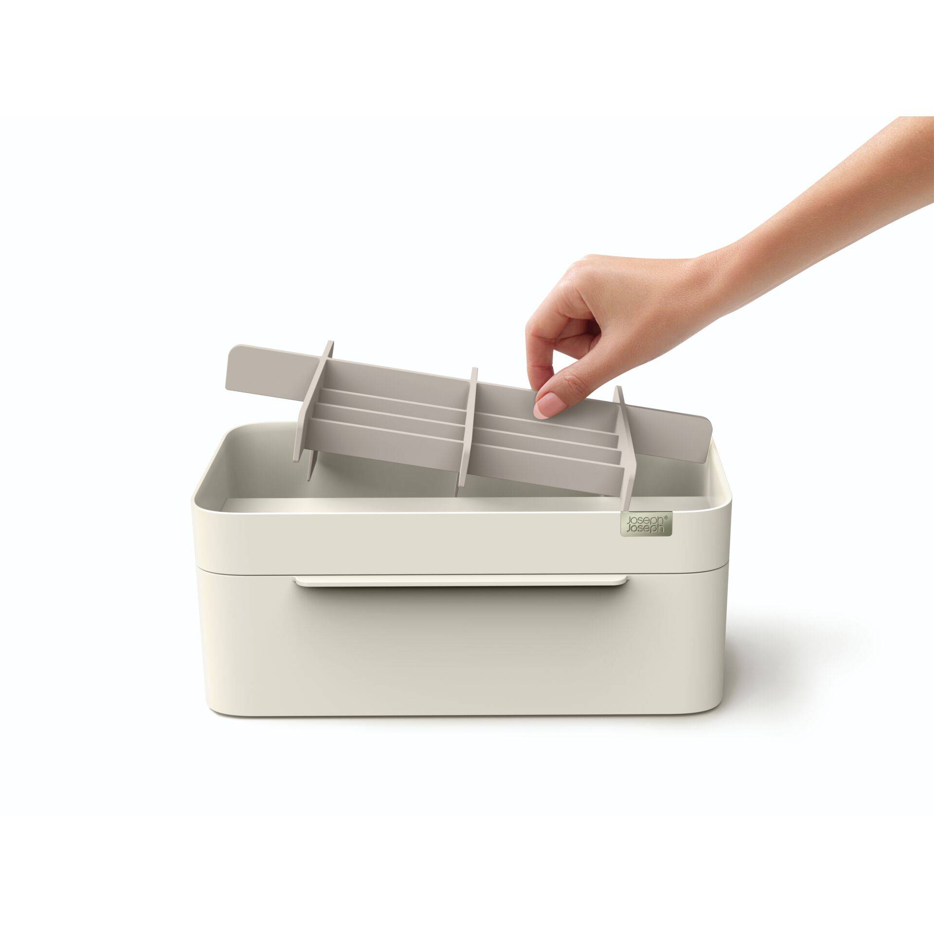 Hand, die ein abnehmbares Tablett in eine beige Aufbewahrungsbox mit offenen Deckel auf weißem Hintergrund platziert.