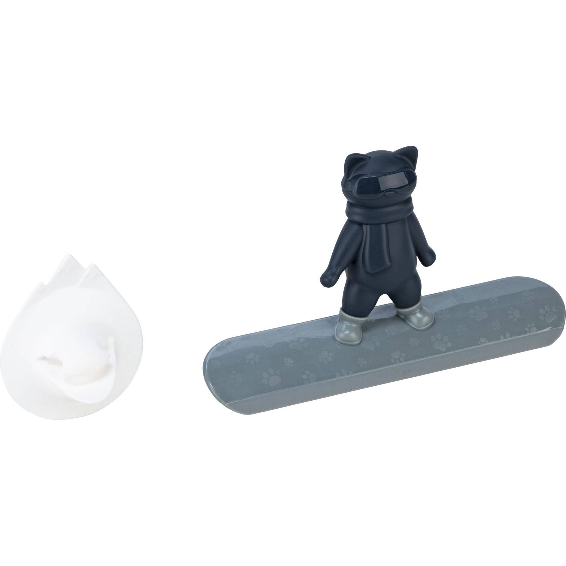 Kleine schwarze Katzenfigur, die auf einem langen grau gemusterten Brett steht, mit einem separaten weißen rissigen schalenartigen oder blütenblattähnlichen Objekt daneben.