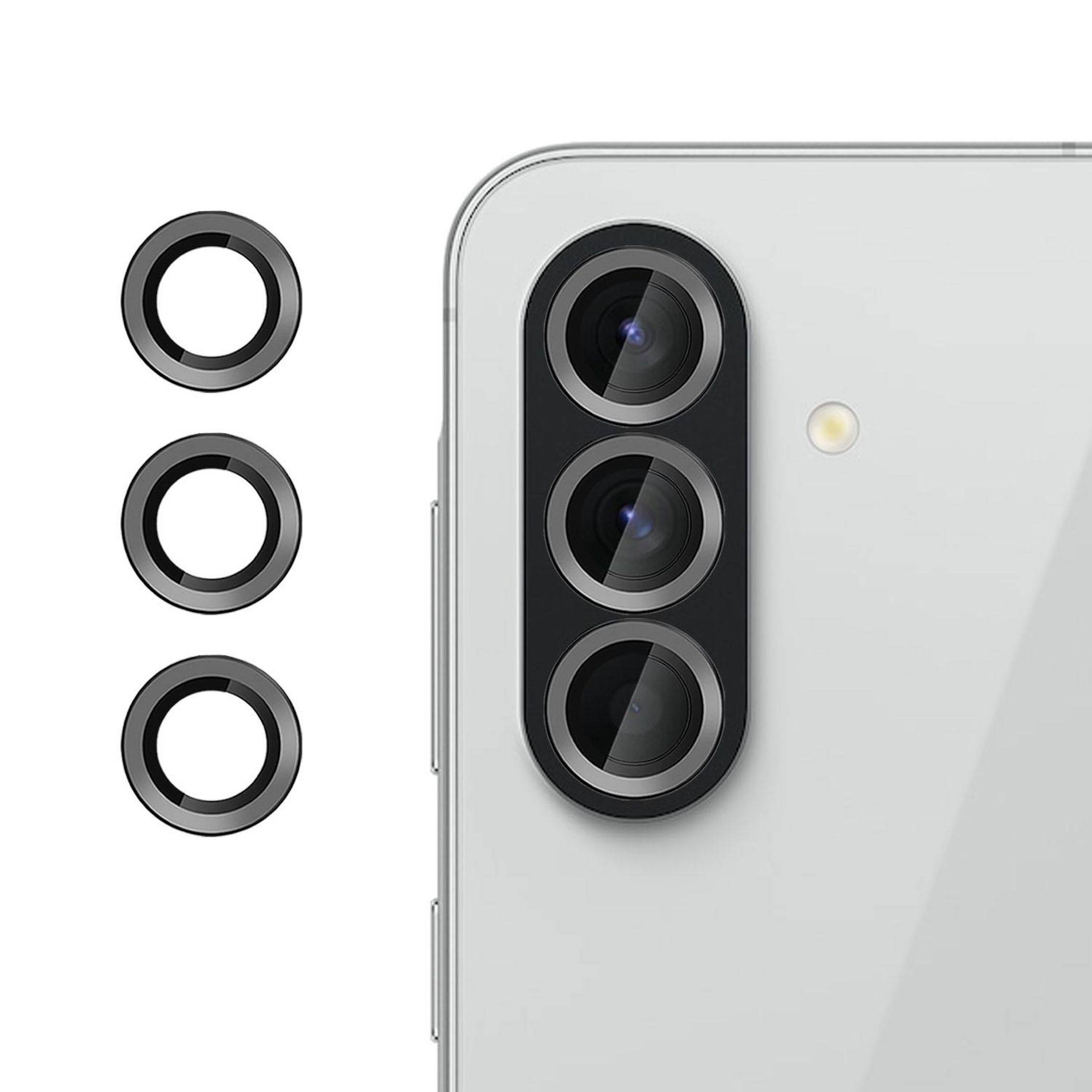 Nahaufnahme eines Smartphone-Rückfahrtkamera-Moduls mit drei Linsen, gezeigt neben drei separaten Metallring-Akzenten auf weißem Hintergrund.