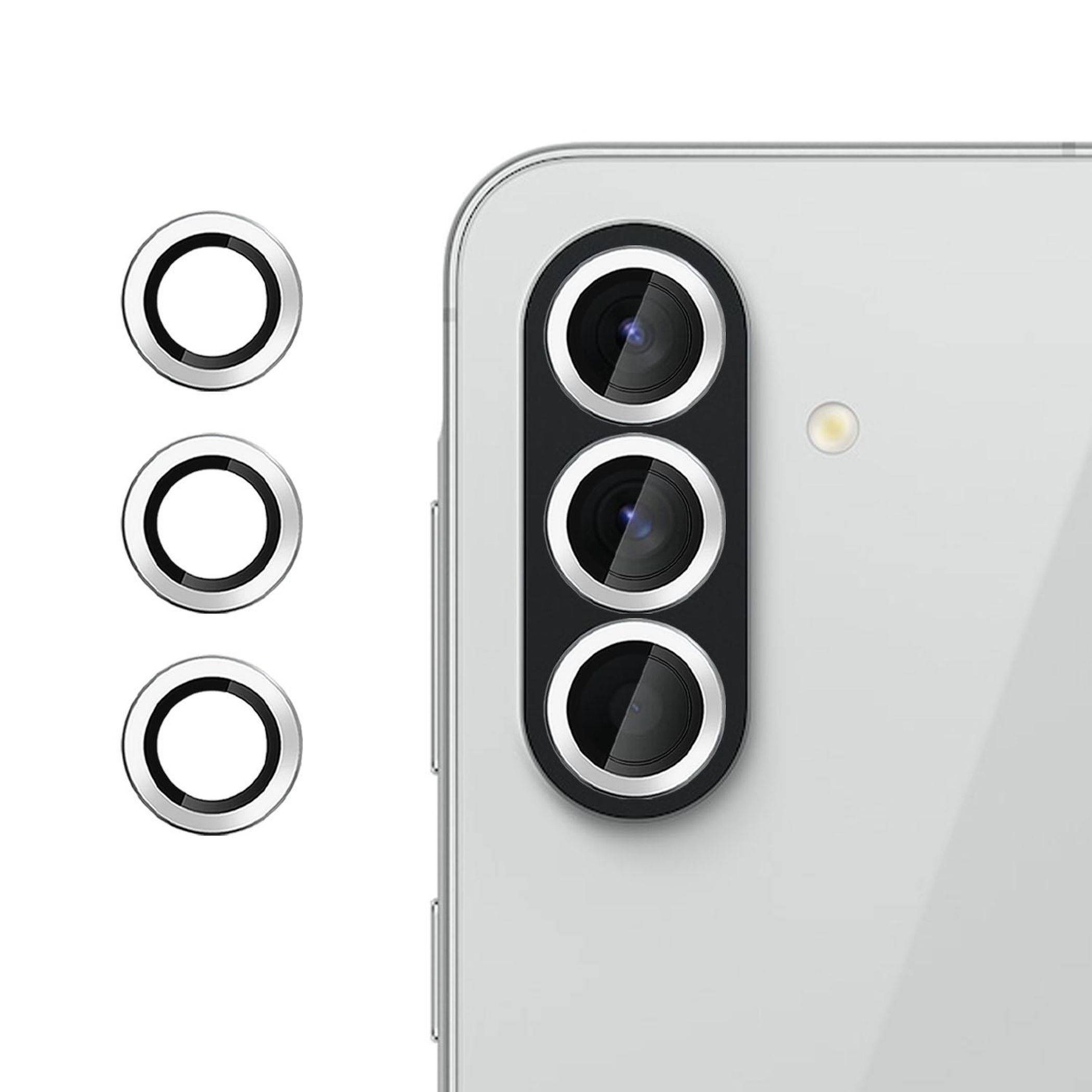 Weißes Smartphone von hinten mit dreifacher Rückkamera und Blitzlicht, plus drei separate kreisförmige Objektivring-Zubehörteile daneben gezeigt.