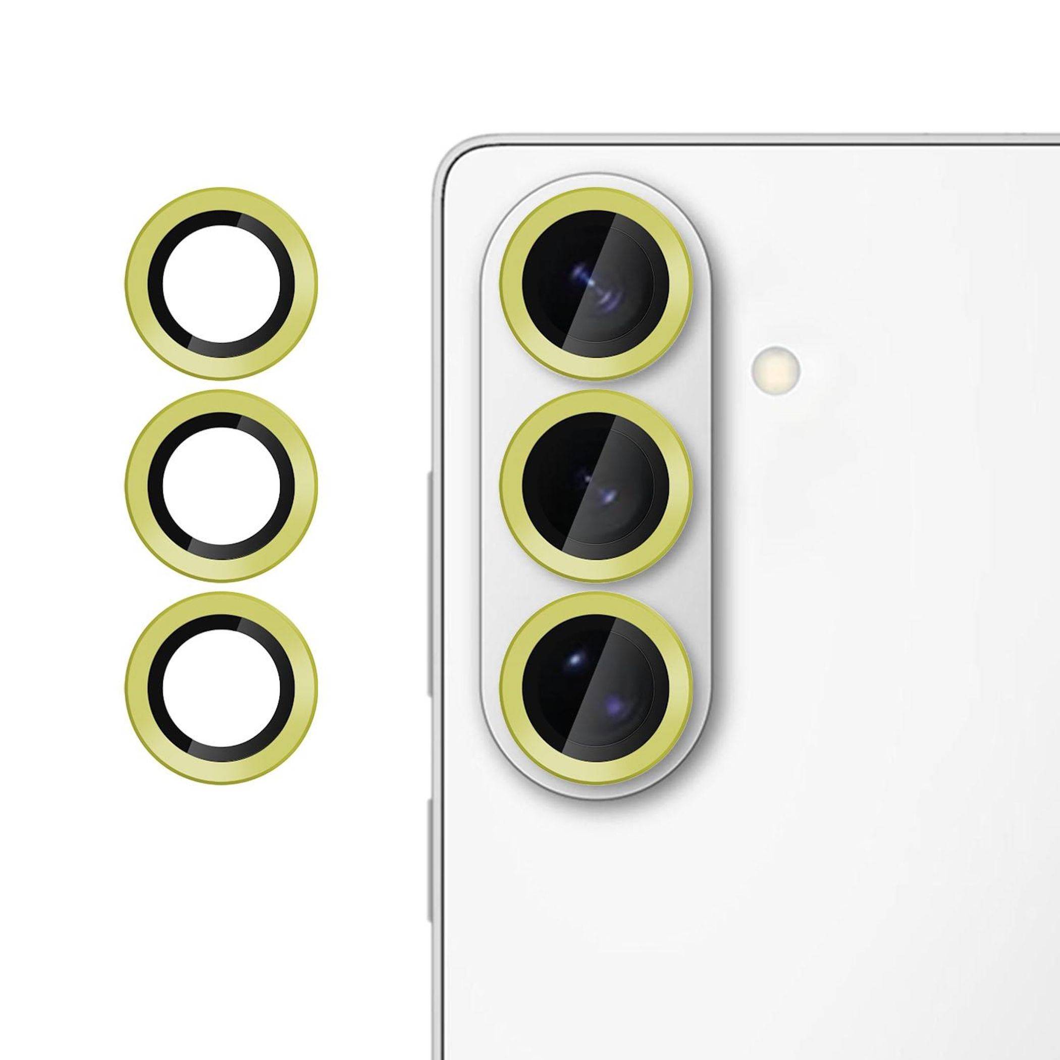 Drei gelbe Kameralinsenringe neben einem weißen Smartphone mit dreifacher Rückfahrtkamera, die austauschbare Linsenschutz-Zubehörteile für das Telefon anzeigen.